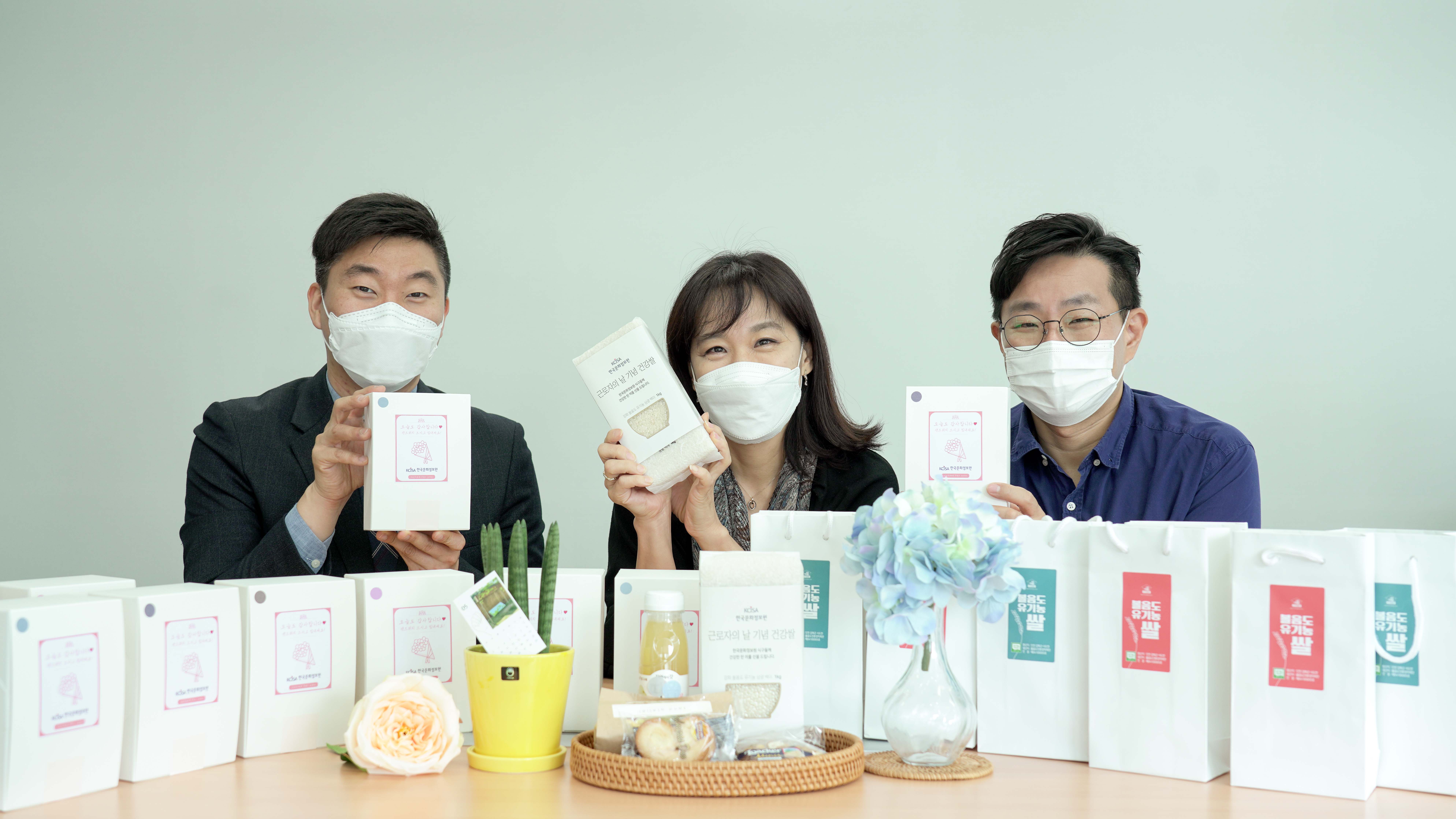 한국문화정보원 홍희경 원장님과 직원들이 근로자의 날 기념으로 샌드위치와 건강 쌀을 들고 웃고 있습니다.